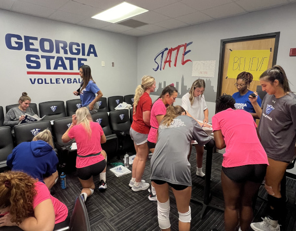 Volleyball players gathered in a team room writing on posters